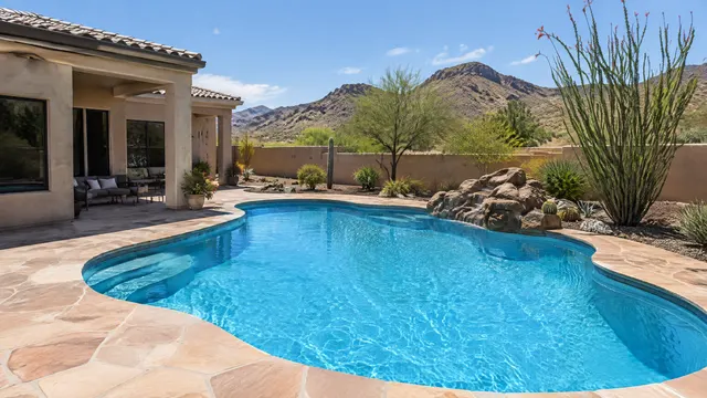 Backyard pool at a 1990s Sonoran-style stucco home in northeast Mesa, Arizona near desert foothills: freshly replastered blue pool, flagstone-look deck, desert landscaping with ocotillo and a view of rocky mountains